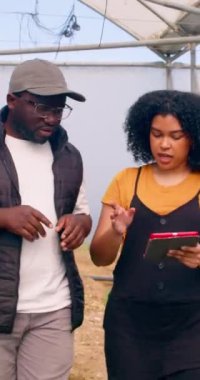 Yürüyen ve konuşan iki siyah çiftçi dijital tabletle veri analizini tartışıyor. Yüksek kalite 4k görüntü