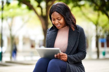 Genç siyahi kadın parkta bankta oturuyor, elinde tablet yüksek kaliteli fotoğraf var.