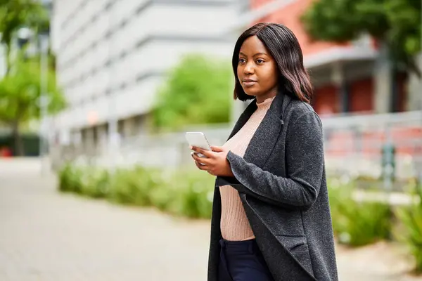 Young Black career woman outside office holding cell phone, trees in background. High quality photo