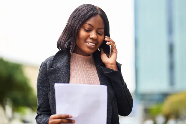 Young Black career woman talking on cell phone, holding document. High quality photo