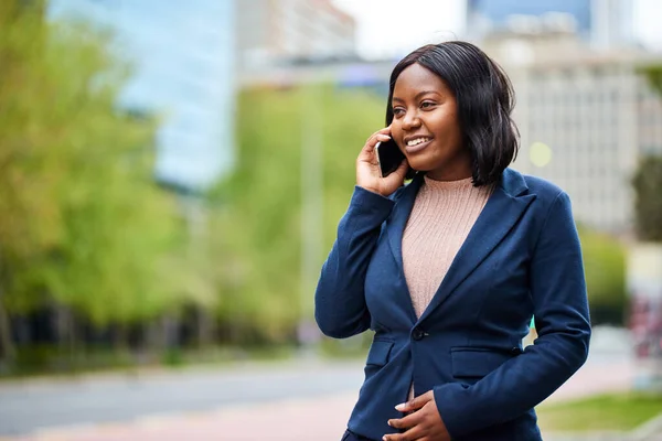 Young Black career woman walking outside while talking on the phone. High quality photo