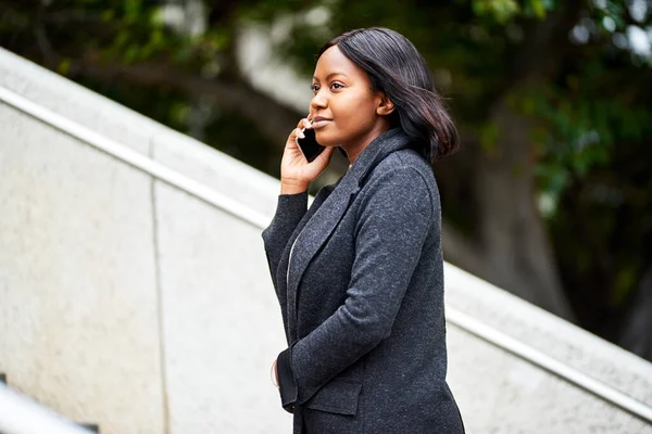 Young Black career woman walking up stairs outside while talking on the phone. High quality photo
