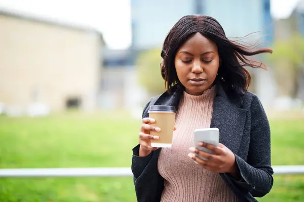 Young Black career woman holding cell phone and takeaway coffee. High quality photo