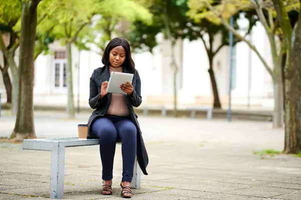 Young Black career woman sitting on outdoor bench with tablet, smiling High quality photo