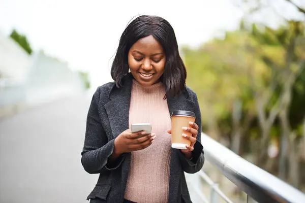 Young Black career woman holding cell phone and takeaway coffee, urban area. High quality photo