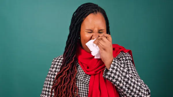 Young Black woman sneezes into tissue, blows nose, sick over Christmas. High quality photo