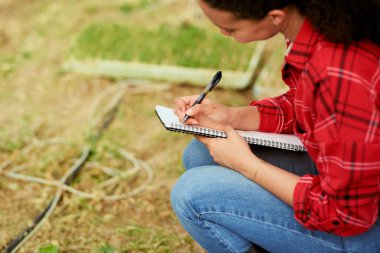 Çok ırklı kadın çiftçi çömeliyor, notlar yazıyor, arka planda ekinler var. Yüksek kalite fotoğraf