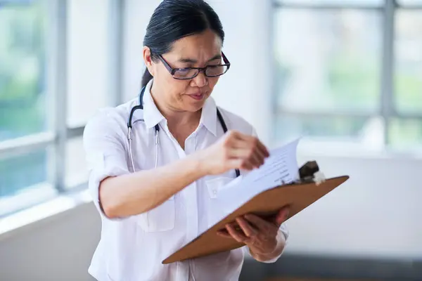 Deneyimli bir tıp uzmanı, parlak ve modern bir hastane ortamındaki hasta kayıtlarını dikkatlice inceliyor. Doktor kaliteli sağlık hizmeti sunmaya odaklanıyor..