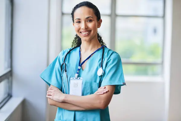 Önlüklü, kendine güvenen, gülümseyen kadın bir doktor kollarını açık hastane koridorunda kavuşturuyor. Bu görüntü, tıp alanındaki profesyonelliği, sağlık hizmetlerini ve çeşitliliği yansıtır..