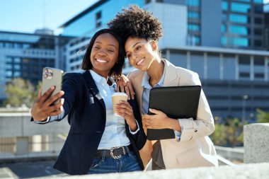 Şehir ortamında iki profesyonel iş kadını dışarıda selfie çekiyor. Bir fincan kahve ve tablet tutuyorlar, çeşitli girişimci ruhu ve modern çalışma kültürünü sergiliyorlar..