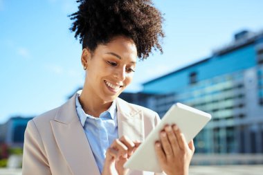 Genç iş kadını şehir ortamında tablet kullanıyor, gülümsüyor ve nişanlı. İş dünyasında modern girişimcilik, teknoloji ve çeşitliliği temsil eder..
