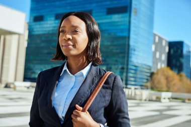 Hırslı ve kendinden emin bir iş kadını modern şehir manzarasında profesyonellik yayarak yürüyor. Resmi iş kıyafeti giymiş, başarıyı ve kararlılığı simgeliyor..