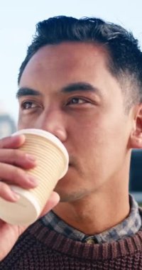 Kısa siyah saçlı, kahverengi kazak giyen yetişkin bir erkek şehirde duruyor ve bir fincan kahvenin tadını çıkarıyor. Bir yudum alır ve düşünceli bir şekilde uzaktaki binalara bakar.