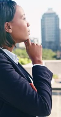 Takım elbiseli genç siyahi bir iş kadını şehirde duruyor, gülümseyerek ve eli çenesinde, ağır çekimde. Hırs ve umut dolu bakışları var..