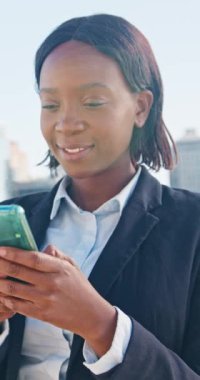 Genç ve profesyonel bir kadın modern bir şehirde akıllı telefon kullanırken gülümsüyor. İş kıyafetleri içinde, özgüven ve başarı havası yayıyor..