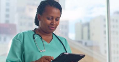 Kendine güvenen bir tıp uzmanı, modern bir hastanenin penceresinin yanındaki bir tablette hasta verilerini kontrol ediyor..