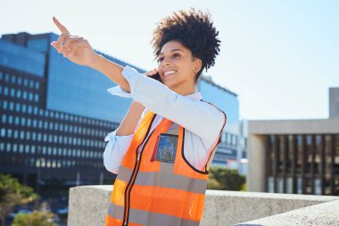 Kendine güvenen kadın inşaat işçisi modern bir binayı işaret ederken yol tarifi veriyor. Kentsel bir ortamda profesyonellik ve takım çalışması.