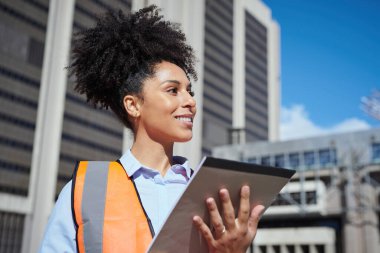 Güler yüzlü kadın inşaat işçisi, şehir merkezinde bir pano tutuyor, güven ve profesyonelliği simgeliyor..