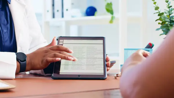 stock image A doctor reviews medical results with a patient using a tablet in a clinical environment, highlighting modern healthcare and patient care technology.