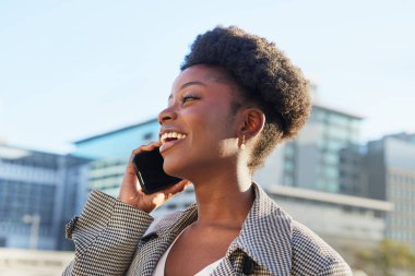 Neşeli bir kadın, şehir ortamında cep telefonuyla konuşurken ışıl ışıl gülümser.. 