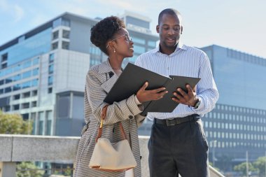 İki profesyonel, modern bir şehir ortamında açık havada odaklanmış bir iş tartışmasına girişiyor. Şirket ortamında işbirliği ve takım çalışmasını öneren belgeleri birlikte gözden geçiriyorlar.. 