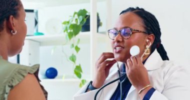 Siyahi bir kadın doktor, hasta kalp atışlarını dinlemek için steteskop kullanır..