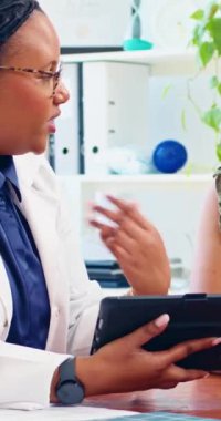 Kadın bir doktor, ofisinde dijital tablet kullanarak hastasına danışmanlık yapıyor..