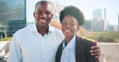 İki mutlu Afrikalı Amerikalı iş arkadaşı kameraya gülümsüyor. Onlar şehirde dışarıda dikiliyorlar. Adamın kolu kadının omzunda..