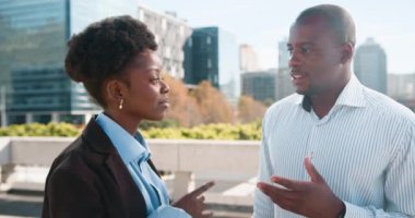 İki iş adamı, resmi olarak giyinmiş bir Afrikalı Amerikalı kadın ve erkek, modern bir şehir ortamında dışarıda tartışıyorlar.