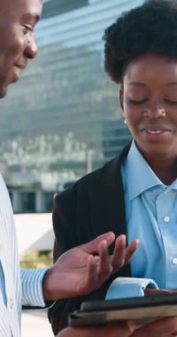 İki Afrikalı Amerikalı iş arkadaşı modern bir ofis binasının dışında tartışıyorlar. İkisi de şık giyinmiş ve kadın tabletinde gösterilen bilgileri tartışırken gülümsüyor..