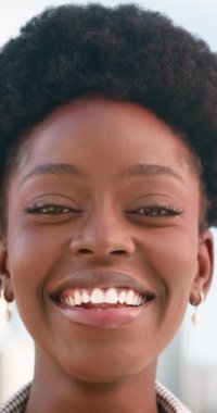 Gülümseyen ve kameraya bakan mutlu Afro-Amerikan bir kadının yakın çekimi. Afro saç stili var ve kareli gömlek giyiyor..