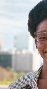 Kendine güvenen siyahi iş kadını şehirdeki kameraya gülümsüyor. Gözlük takan ve iş kıyafetleri içinde gülümseyen Afrikalı bir Amerikalı kadın. 