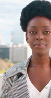 Genç, şık ve kendine güvenen siyahi bir kadın modern bir şehir manzarasına karşı duruyor. Doğrudan kameraya bakıyor, gözleri güç ve hırs taşıyor.