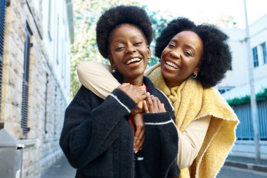 Güneşin altında şehrin bir caddesinde dikilen iki neşeli arkadaş. Her iki kadın da parlak bir şekilde gülümsüyor, yakın arkadaşlar arasındaki samimiyet ve arkadaşlığı sergiliyorlar.. 