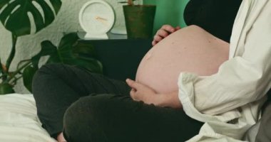 Hamile bir kadın yatağında oturur ve büyük karnını sevgiyle okşar. O, siyah bir sütyen ve beyaz bir gömlek giyiyor. Ana fikir, bir annenin doğmamış çocuğunu sevmesidir..