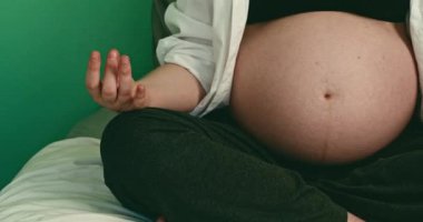 Pijamalı hamile bir kadın yatakta yoga yapıyor. Hamilelik boyunca huzur ve rahatlama kavramı. Bir kadın meditasyon yapar ve zihinsel ve fiziksel sağlığıyla ilgilenir..