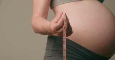 Hamile kadın göbeğini ölçüyor. Hamile bir kadın bebeğinin şişkinliğinin boyutunu ölçer. Annelik, hamilelik, sağlık ve annelik kavramları. Hamile karnına yakın plan..