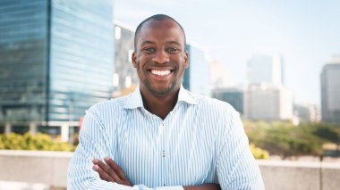 A confident, smiling professional posing outdoors in an urban setting, surrounded by modern skyscrapers and urban greenery under a bright, clear sky. clipart