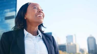 Açık havada, açık ve aydınlık bir günde şehrin arka planında duran kendine güvenen bir iş kadını gülümsüyor..