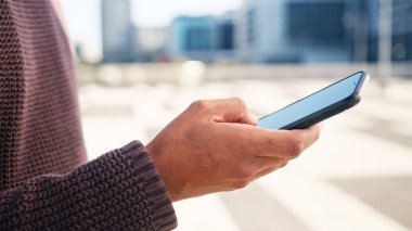 Şehir ortamında akıllı telefon kullanan bir kişinin yakın çekim görüntüsü, iletişim ve teknolojiyi ön plana çıkarıyor..