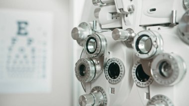 Detailed photograph of optometry equipment used for eye exams with a blurred eye chart in the background, symbolizing vision care and precision in ophthalmology settings. clipart