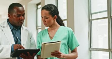 Bir erkek doktor ve bir kadın hemşire hasta bilgilerini hastane koridorunda bir tablet ve not defteri kullanarak tartışırlar. Verimli tedavi için sağlık ortamında işbirliği.