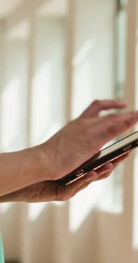 Perdeleri sade bir şekilde aydınlatılmış bir odada akıllı telefonunu kullanan ve ekranda kaydırıp tıkırdatırken rahatlık ve rahatlık hissi veren bir insanın yakın çekimi..