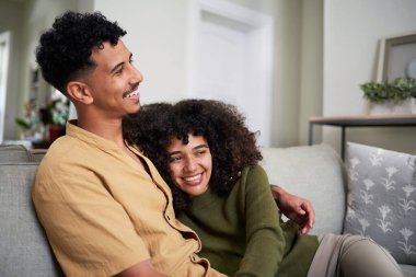 Neşeli bir çift rahat rahat oturma odalarında oturuyorlar. Sıcak bir şekilde gülümsüyorlar ve mutlu görünüyorlar. Birlikte huzurlu ve mutlu bir anı paylaşıyorlar..