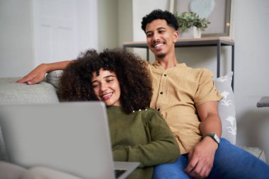 Genç ve neşeli bir çift rahat bir kanepede dizüstü bilgisayar kullanarak rahatlıyor. Sıcak ve davetkar bir ortamda kahkaha ve neşe anlarını paylaşıyorlar. Boş zamanın ve bağlantının mükemmel temsilidir.