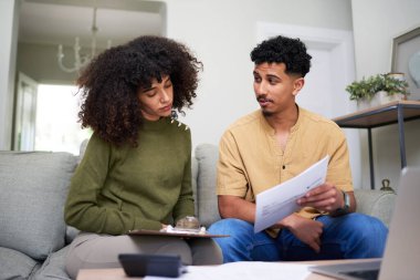 Genç bir çift rahat oturma odalarında oturmuş evrakları dikkatle gözden geçiriyor ve mali konuları tartışıyorlar. Rahatlamış ortam, kişisel finans yönetimi ve ilişki takım çalışmasında işbirliği gösteriyor.