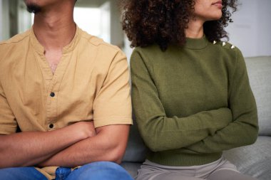 Kanepede oturan bir çiftin yakın plan görüntüsü çapraz kollarla, insanlar arası anlaşmazlığı ya da anlaşmazlığı simgeliyor. Görüntü, günlük ev ortamında duygusal gerilim ve gergin ilişki dinamiklerini yakalıyor..