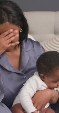 Pijamalı yorgun bir anne yatağa oturur ve bebeğini kucağına alır. Alnını ovuyor, gözlerini kapıyor ve bitkinmiş gibi iç çekiyor. Bebek kameradan uzağa bakıyor. Kadın siyahi, muhtemelen Afro-Amerikalı..