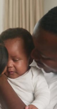 Sevgi dolu bir Siyah aile evde kaliteli vakit geçirmekten hoşlanır. Anne ve baba sevimli bebeklerini sevgi, öpücük ve kucaklaşma yağmuruna tutarlar. Bebek merakla kameraya bakıyor, aile bağlarının ve mutluluğun iç açıcı bir anını yakalıyor..