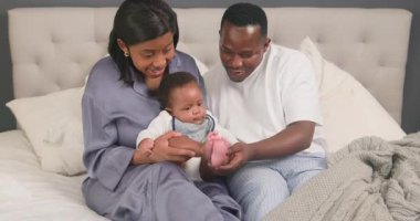 Sevgi dolu bir siyahi aile, yatak odalarında birlikte vakit geçirmekten zevk alır. Baba bebek ayaklarıyla nazikçe oynarken anne de sevimli bebeğini kucağına alıyor. Bu iç açıcı sahne aile bağlarının ve aile sevgisinin özünü yansıtıyor..